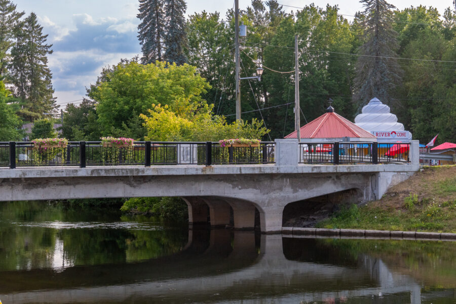 Concrete bridge with flower planters over the Gull River, with River Cone ice cream stand in the background, Minden Ontario